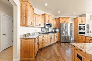 Kitchen with a textured ceiling, dark hardwood / wood-style flooring, stainless steel appliances, and light stone counters