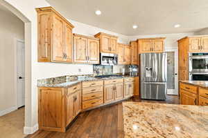 Kitchen featuring appliances with stainless steel finishes, a textured ceiling, dark hardwood / wood-style flooring, and stone countertops