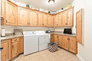 Clothes washing area featuring cabinets, a textured ceiling, light tile patterned floors, and washing machine and clothes dryer