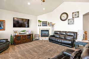 Carpeted living room with lofted ceiling, ceiling fan, and a fireplace