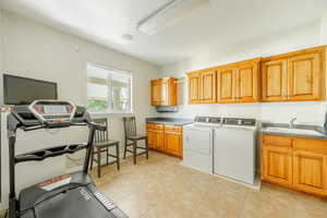 Laundry room with washing machine and dryer, light tile patterned flooring, sink, and cabinets