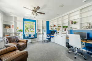 Office area featuring ceiling fan, built in shelves, ornamental molding, built in desk, and light carpet