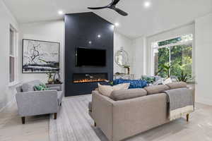 Living room featuring ceiling fan, vaulted ceiling, light hardwood / wood-style floors, and a fireplace