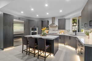 Kitchen with a center island, a breakfast bar area, sink, wall chimney range hood, and appliances with stainless steel finishes