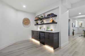 Bar featuring beverage cooler, light hardwood / wood-style floors, dark brown cabinetry, and a barn door