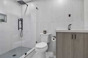 Bathroom featuring tile walls, an enclosed shower, vanity, and toilet