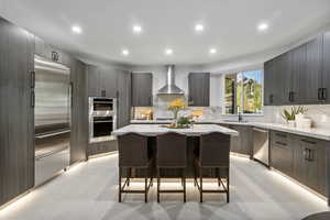 Kitchen with sink, wall chimney range hood, appliances with stainless steel finishes, a center island, and a breakfast bar area