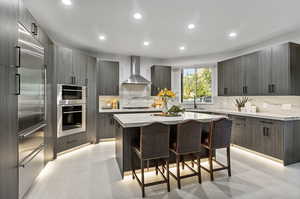 Kitchen with appliances with stainless steel finishes, a kitchen breakfast bar, tasteful backsplash, a kitchen island, and wall chimney range hood