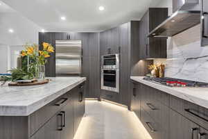 Kitchen featuring decorative backsplash, wall chimney exhaust hood, stainless steel appliances, and light stone counters