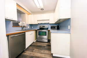 Kitchen with sink, a textured ceiling, white cabinetry, stainless steel appliances, and dark hardwood / wood-style flooring