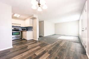 This view shows the kitchen, dining area the formal front room and the entrance to outside to the right.  Kitchen with a textured ceiling, white cabinetry, stainless steel appliances, dark LVP / wood-style floors, and a notable chandelier