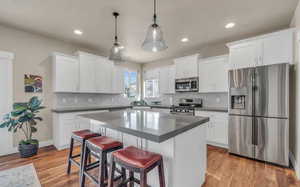 Kitchen featuring white cabinets, pendant lighting, a kitchen island, stainless steel appliances, and light hardwood / wood-style floors