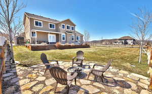 Rear view of property featuring a patio, a yard, and a fire pit