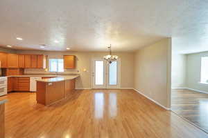 Kitchen with kitchen peninsula, white appliances, a textured ceiling, a chandelier, and light wood-type flooring