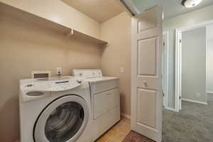 Washroom with a textured ceiling, light colored carpet, and washer and clothes dryer