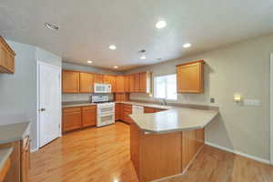 Kitchen with light wood-type flooring, white appliances, sink, and kitchen peninsula