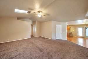 Unfurnished living room with a textured ceiling, ceiling fan with notable chandelier, lofted ceiling with skylight, and carpet