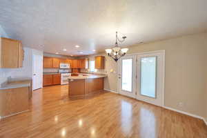 Kitchen with hanging light fixtures, white appliances, a textured ceiling, an inviting chandelier, and light hardwood / wood-style flooring