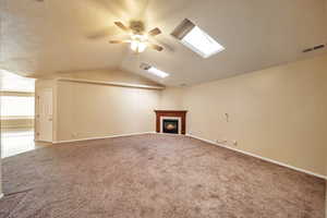 Unfurnished living room with ceiling fan, carpet flooring, and lofted ceiling with skylight