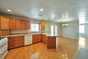 Kitchen with white appliances, kitchen peninsula, light hardwood / wood-style flooring, sink, and a chandelier