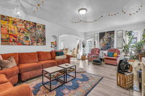 Spacious living room, 1st Unit, featuring a notable chandelier, a textured ceiling, and light hardwood / wood-style floors