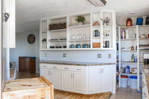 Interior space featuring light wood-type flooring, a textured ceiling, white cabinetry, and light stone countertops