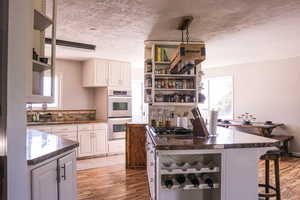 Kitchen with light hardwood / wood-style flooring, white cabinets, a textured ceiling, and appliances with stainless steel finishes