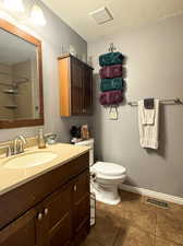 Bathroom with vanity, toilet, a textured ceiling, walk in shower, and tile patterned flooring