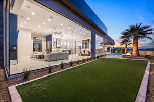 Yard at dusk with a patio area, ceiling fan, and an outdoor living space with a fire pit