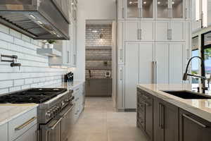 Kitchen with light stone counters, sink, backsplash, and stainless steel range