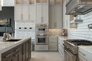 Kitchen with wall chimney range hood, sink, decorative backsplash, light stone countertops, and stainless steel appliances