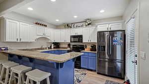 Kitchen with a breakfast bar, white cabinetry, light hardwood / wood-style flooring, black appliances, and blue cabinets