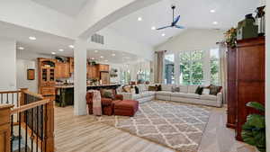 Living room with ceiling fan with notable chandelier, lofted ceiling, and light hardwood / wood-style flooring