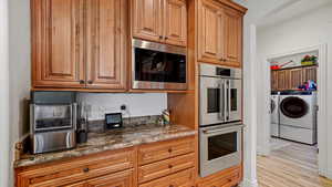 Kitchen featuring dark stone counters, appliances with stainless steel finishes, light hardwood / wood-style flooring, and washer and dryer