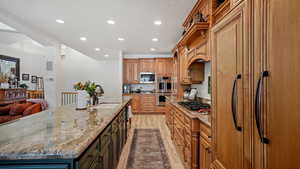 Kitchen featuring light hardwood / wood-style floors, built in appliances, a large island with sink, sink, and light stone countertops