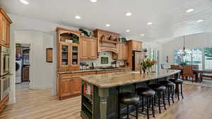 Kitchen with light wood-type flooring, a chandelier, a center island with sink, and stainless steel appliances