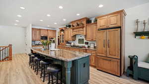 Kitchen featuring light stone countertops, a center island with sink, light wood-type flooring, and stainless steel appliances