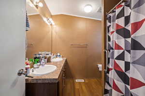 Bathroom with wood-type flooring, vaulted ceiling, walk in shower, crown molding, and vanity