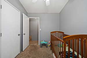 Carpeted bedroom featuring ceiling fan and a nursery area