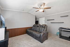 Carpeted living room with ornamental molding, wooden walls, lofted ceiling, and ceiling fan