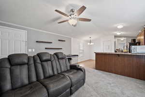 Carpeted living room featuring ceiling fan with notable chandelier, lofted ceiling, a textured ceiling, and ornamental molding