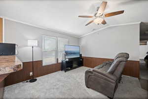 Living room featuring crown molding, lofted ceiling, wood walls, and ceiling fan