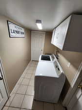 Clothes washing area featuring separate washer and dryer, cabinets, and light tile patterned floors