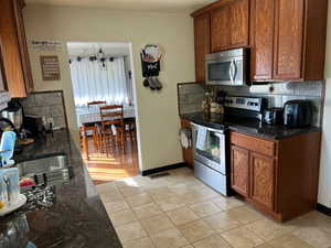 Kitchen featuring appliances with stainless steel finishes, tasteful backsplash, light hardwood / wood-style flooring, dark stone counters