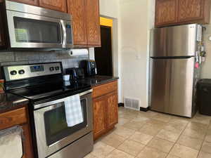 Kitchen featuring appliances with stainless steel finishes, backsplash, light tile patterned floors, and dark stone counters