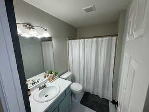 Guest Bathroom with a textured ceiling, curtained shower, vanity, and toilet