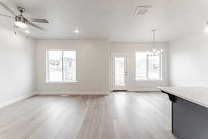 Interior space with light hardwood / wood-style flooring, ceiling fan with notable chandelier, a wealth of natural light, and a textured ceiling