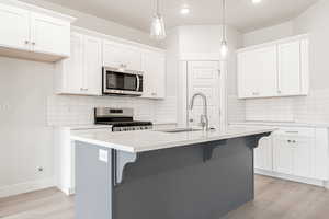 Kitchen with appliances with stainless steel finishes, a kitchen island with sink, and white cabinets