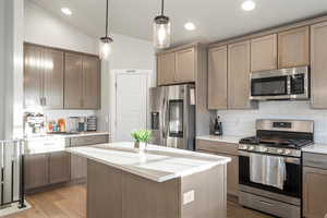 Kitchen featuring light hardwood / wood-style floors, vaulted ceiling, backsplash, stainless steel appliances, and decorative light fixtures