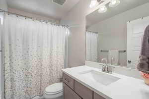 Full bathroom on main floor with vanity, lofted ceiling, toilet, and curtained shower